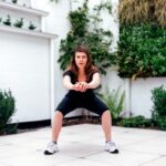 Femme effectuant un squat dans un jardin, séance type proposée par un coach sportif en vidéo